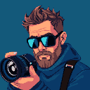 A photographer with a beard, sunglasses, and an undercut hairstyle holds a professional camera.