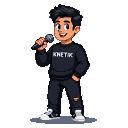 Tanned young man with styled black hair, wearing a "KNETIK" pixelated jumper and dark pants, holds a microphone to his lips mid-performance.